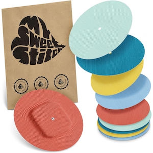 Może przedstawiać: Stos kolorowych, teksturowanych, owalnych plastrów medycznych w odcieniach niebieskiego, żółtego i czerwonego, z brązową papierową torbą z napisem "My Sweet Stitch". Torba ma trzy okrągłe pieczęcie z tekstem.