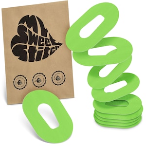 May include: A collection of vivid green, oval medical patches with a central aperture, alongside a brown paper packet. The packet displays a black heart-shaped logo with the words "My Sweet Stitch" and three circular seals.