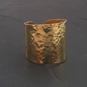 May include: A gold hammered metal cuff bracelet. The bracelet is wide and has a textured surface.