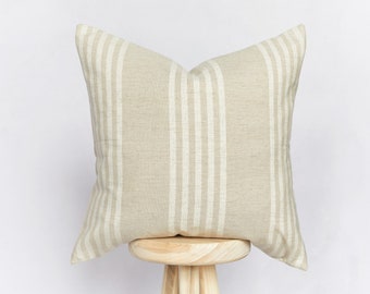 May include: A beige and white striped throw pillow with a linen texture. The pillow is sitting on a wooden stool.