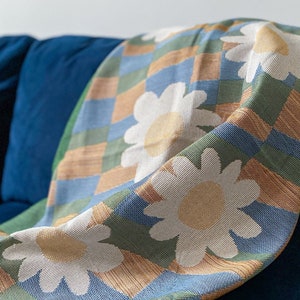 May include: A blue, green, and brown throw blanket with a checkered pattern and white daisy flowers.