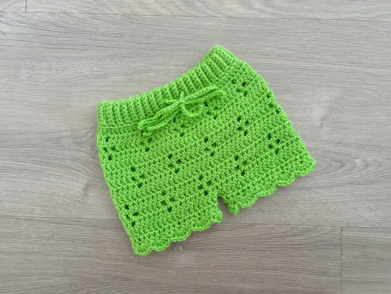 Op de afbeelding: Groene gehaakte shorts met een gegolfde zoom en een strik in de taille.