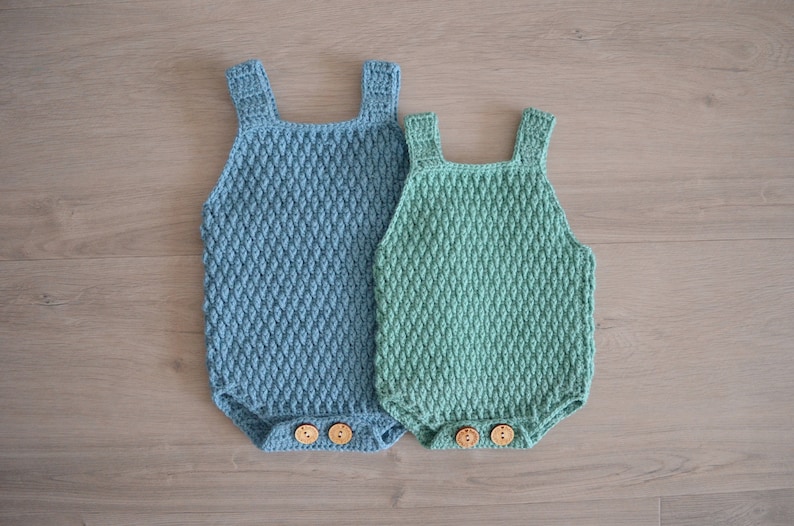 May include: Two crocheted baby onesies, one blue and one green, with wooden buttons.