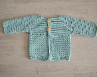 May include: A light blue crocheted cardigan with wooden buttons. The cardigan has long sleeves and a button-up front.