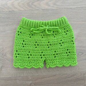Op de afbeelding: Groene gehaakte shorts met een gegolfde zoom en een strik in de taille.