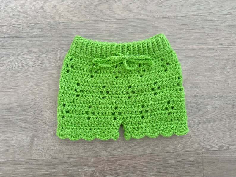 Op de afbeelding: Groene gehaakte shorts met een gegolfde zoom en een strik in de taille.