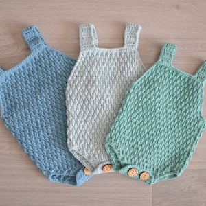 Puede incluir: Tres bodies de bebé de crochet en diferentes colores: azul claro, gris y verde. Cada body tiene cierre de botón y un patrón texturizado.