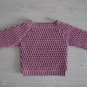 May include: A mauve crocheted sweater with long sleeves and a round neckline.