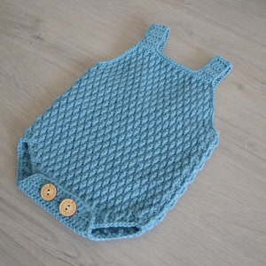May include: A blue crocheted baby onesie with two wooden buttons.