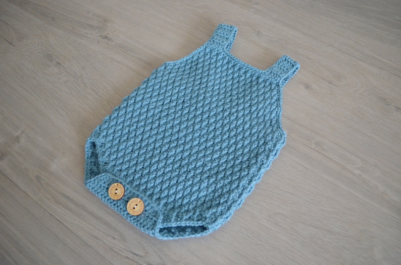 May include: A blue crocheted baby onesie with two wooden buttons.