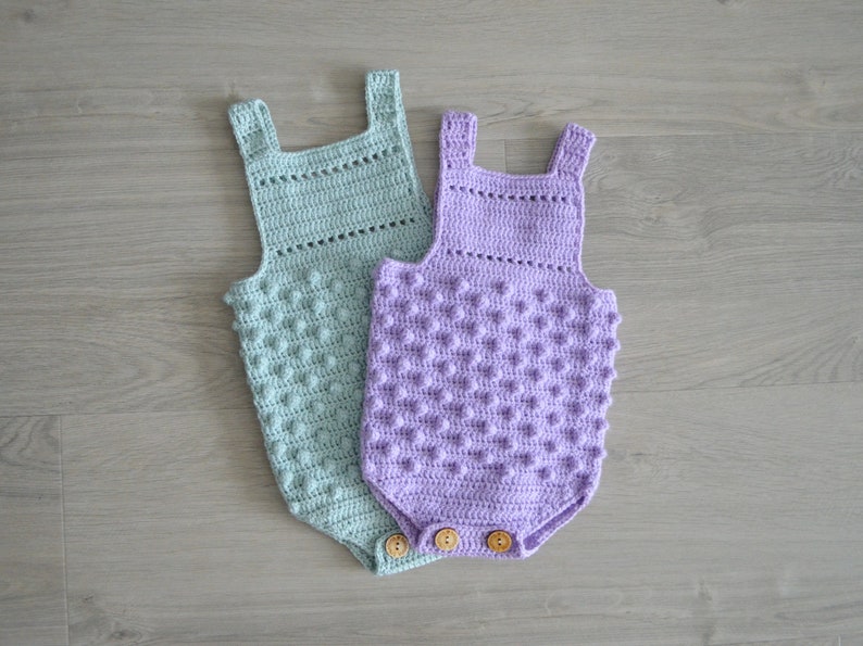 May include: Two crocheted baby onesies, one in light green and one in lavender, with a textured, bumpy design. Both onesies have wooden buttons.