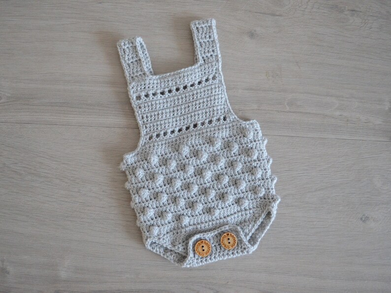 May include: A gray crocheted baby onesie with a textured design and two wooden buttons.