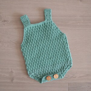 May include: A crocheted baby onesie in a light green color with two wooden buttons.