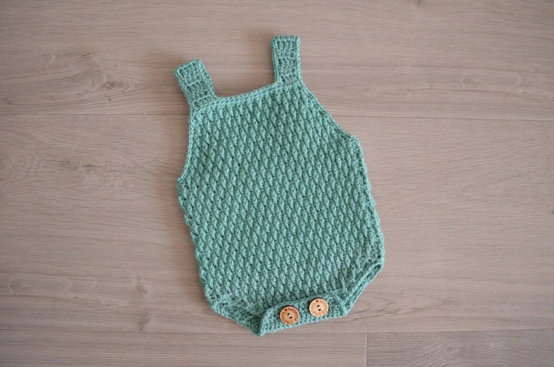 May include: A crocheted baby onesie in a light green color with two wooden buttons.