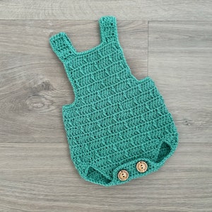 Può includere: Un body per neonato in crochet color turchese con due bottoni in legno.