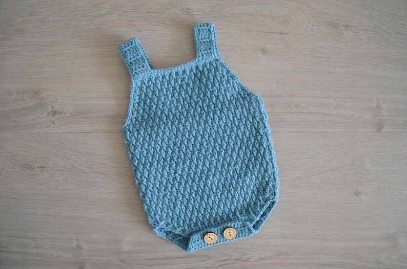 May include: A light blue crocheted baby onesie with wooden buttons.