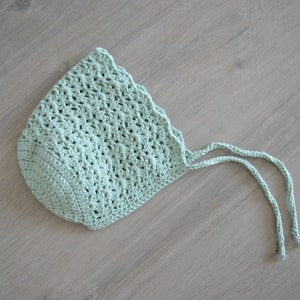 May include: A light green crocheted baby bonnet with two long ties.