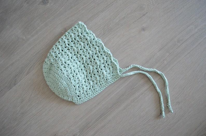 May include: A light green crocheted baby bonnet with two long ties.
