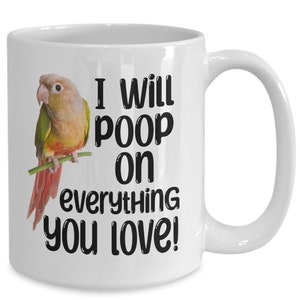 May include: White ceramic coffee mug featuring a green and orange parrot perched on a branch. The mug has black text that reads "I will poop on everything you love!"