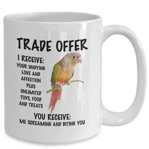 May include: White ceramic mug featuring a green and red parakeet perched on a branch. The mug has black text that reads "TRADE OFFER I RECEIVE: YOUR UNDYING LOVE AND AFFECTION PLUS UNLIMITED TOYS, FOOD AND TREATS YOU RECEIVE: ME SCREAMING AND BITING YOU"