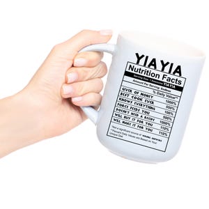 May include: A white ceramic mug featuring a black printed nutrition facts label that reads YIAYIA Nutrition Facts, listing attributes like Giver of Money, Best Cook Ever, Knows Everything, Force Feeds You, and other humorous daily values.