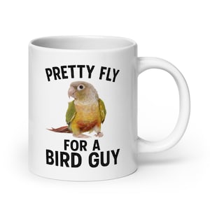 May include: White ceramic mug with the text "PRETTY FLY FOR A BIRD GUY" in black. The mug features a colorful illustration of a small parrot with green, yellow, and red feathers. The mug has a white handle.