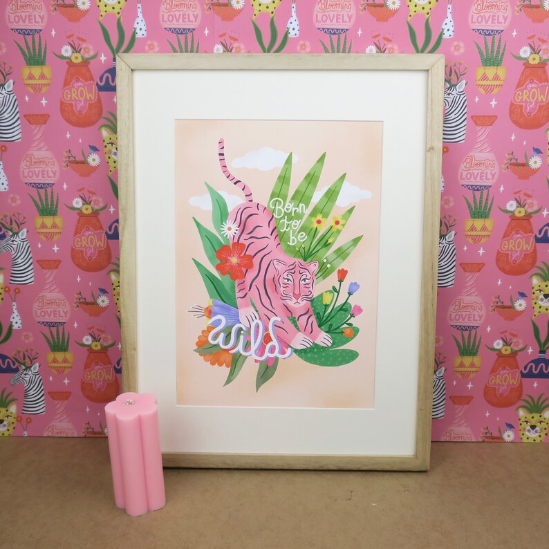 May include: A framed print with a pink tiger in a jungle setting. The tiger is surrounded by green leaves and flowers. The text "Born to be wild" is written in pink letters below the tiger.