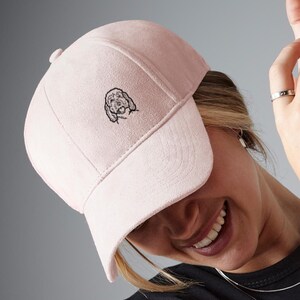 May include: A pink suede baseball cap with a black embroidered dog on the front.