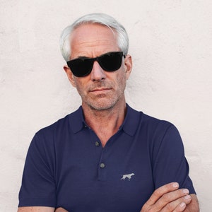 May include: A man wearing black sunglasses and a navy blue polo shirt with a small grey dog logo on the left chest.