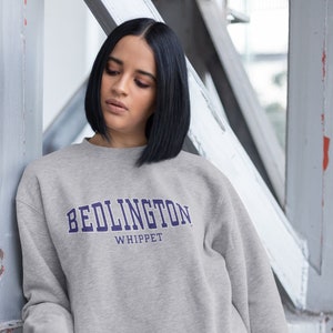 Puede incluir: Una sudadera gris con el texto "Bedlington Whippet" en letras moradas.