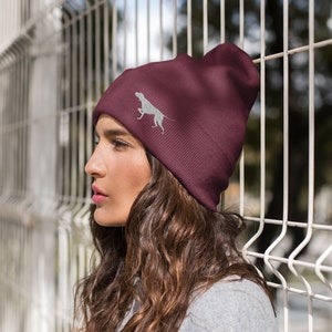 May include: A maroon beanie with a white embroidered silhouette of a dog on the front.