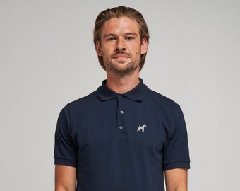 May include: A navy blue polo shirt with short sleeves and a classic collar. The shirt has a small, embroidered dog silhouette on the chest. The model is wearing a silver watch and beige trousers. The shirt has three buttons at the neckline.