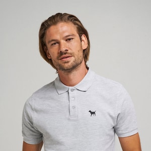 Könnte beinhalten: Ein graues, kurzärmeliges Poloshirt mit einem kleinen schwarzen Hunde-Logo auf der linken Brust.