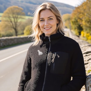 May include: Black fleece jacket with a high collar, a front zipper, and a small pocket on the chest. A white dog silhouette is embroidered on the left chest. The jacket is worn with blue jeans.