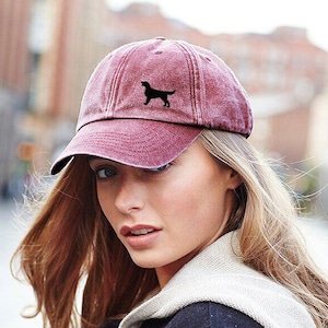 May include: A maroon baseball cap with a black dog silhouette embroidered on the front. The cap has a curved brim and a slightly faded appearance. The hat is a casual accessory.
