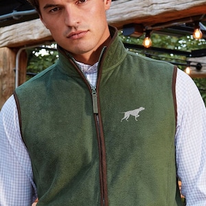 Peut inclure: Une veste en polaire verte avec des bordures brunes et une fermeture éclair. La veste a une petite image brodée d'un chien sur le devant.