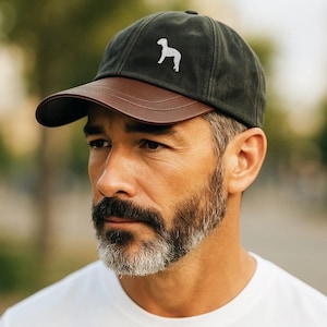 May include: A dark green baseball cap with a brown leather peak. The cap has a white embroidered dog silhouette. The cap is worn by a person.