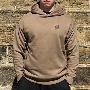 Op de afbeelding: Een bruin hoodie met een klein geborduurd hondenontwerp op de voorkant.