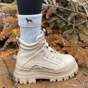 May include: Light grey socks featuring a black dog silhouette, paired with beige platform boots. The boots have a chunky sole and a high-top design. The socks are folded over the top of the boots.