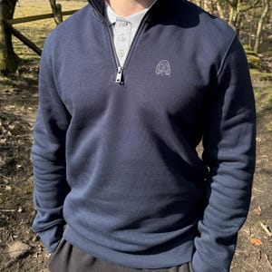 May include: A navy blue quarter-zip sweatshirt with a small embroidered dog design on the left chest.