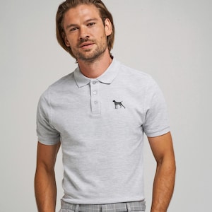 May include: Light gray polo shirt with a black dog silhouette on the chest. The shirt has a classic collar and three-button placket. The model is wearing gray and white plaid pants.