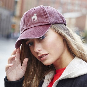 May include: A burgundy baseball cap with a distressed look and a white silhouette of a dog on the front.