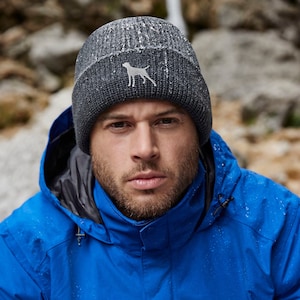 May include: A man wearing a blue jacket with a gray knit beanie featuring a small dog logo. The beanie has a textured, flecked appearance.