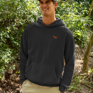 May include: A black hooded sweatshirt with a small embroidered brown dog on the left chest. The model is wearing a green baseball cap with a brown dog embroidered on the front.