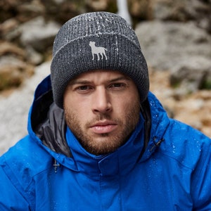 Puede incluir: Un hombre con una chaqueta azul y una boina gris oscuro con un logotipo de perro blanco. La boina tiene una textura acanalada.