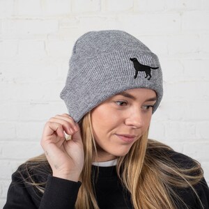 May include: A gray knit beanie with a black embroidered silhouette of a dog on the front.