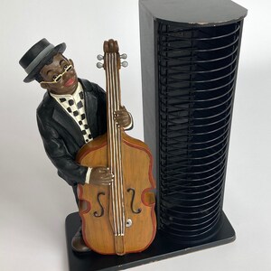 Pu&ograve; includere: Una torre per CD nera con una statuetta di un uomo che suona il basso. La statuetta &egrave; in resina dipinta ed &egrave; in posizione eretta. La torre ha una struttura in metallo nero e pu&ograve; contenere fino a 72 CD.