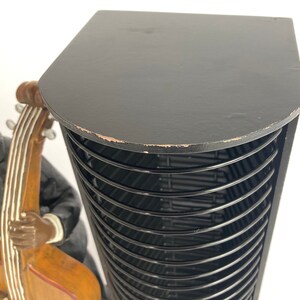 Pu&ograve; includere: Torre porta CD nera con un piano in legno e una struttura in metallo nero. La torre &egrave; piena di fessure nere per CD. In primo piano c'&egrave; una statuetta di una persona che suona il basso.