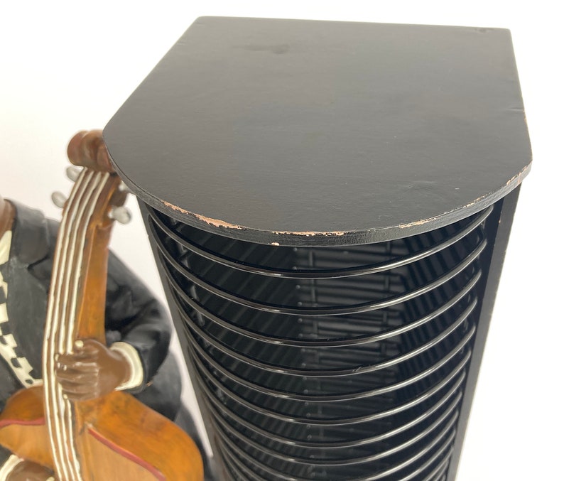 Pu&ograve; includere: Torre porta CD nera con un piano in legno e una struttura in metallo nero. La torre &egrave; piena di fessure nere per CD. In primo piano c'&egrave; una statuetta di una persona che suona il basso.