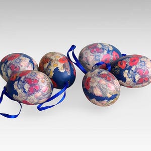 Puede incluir: Seis huevos de Pascua azules decorados con diseños florales y de mariposas. Los huevos están adornados con flores y mariposas rojas, rosas y blancas. Los huevos están atados con una cinta azul.